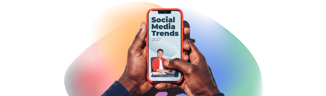 Hands holding a smartphone displaying a Social Media Trends 2027 screen with a man sitting at a desk.