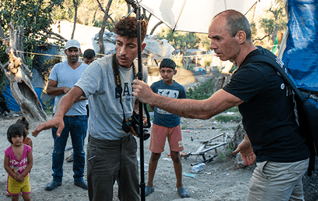 a photograph is being helped by his assistant to take photos of refugees